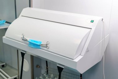 Tıbbi bir odada sterilizasyon ünitesi. Mavi steril bez tutan kıskaçlar var. Bu teçhizat, cerrahi prosedürler için steril bir ortamın bakımını sağlar.