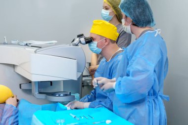 Koruyucu kıyafetli cerrahi ekip özel bir mikroskop kullanan bir cerrah tarafından yapılan lazer göz ameliyatını yönetiyor. Ekipman ve steril kurulum hastanın güvenliğini sağlar