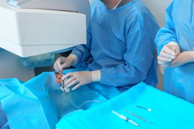 Mavi koruyucu giysili bir cerrah titiz bir göz ameliyatı yapar. Özel aletlerle steril klinik ortamda hassasiyet sağlar.