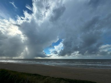 Okyanus dalgalarından yansıyan ve sakin bir kıyı manzarası yaratan dramatik bulutlar ve güneş ışığıyla güzel bir sahil manzarası.