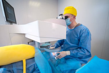 Gelişmiş ekipmanlarla göz ameliyatı yapan bir cerrahın yakın çekimi. Hasta koruyucu kılıflarla hazırlandı ve lazer cihazının altına yerleştirildi.