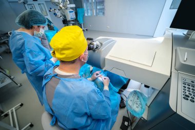 Mavi önlük ve parlak sarı başlık takan kendini işine adamış bir sağlık çalışanı modern bir tıbbi tesiste çalışıyor.