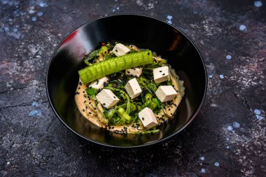 Tofu küpleri, deniz yosunu, salatalık ve susam tohumlarından oluşan canlı bir vejetaryen salatası taze ve sağlıklı bir yemek seçeneği sunuyor.