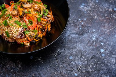 Karışık deniz ürünleri, renkli sebzeler ve susam tohumlu, Asya 'dan esinlenilmiş canlı bir yemek için taze otlarla süslenmiş lezzetli bir kase kızarmış cam erişte.