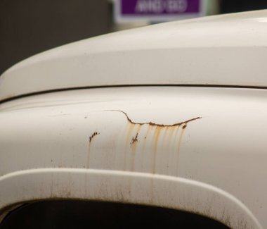 Beyaz bir iş kamyonunun çamurluğunda paslı bir çizik.