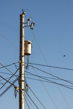 Mavi gökyüzü arka planında elektrik hatları ve elektrik direği.