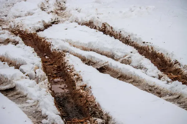 Kışın karla kaplı bir garaj yolunda çamurlu lastik izleri