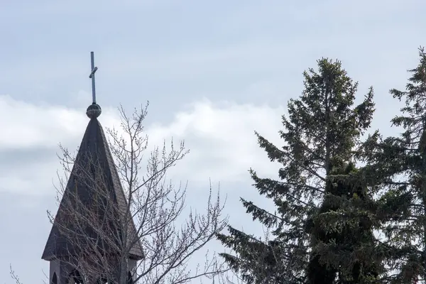 Ormanın arka planında haçı olan bir kilise ve bulutlu bir gökyüzü.