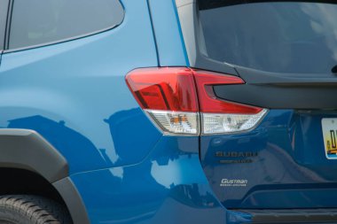 Arabanın yanında siyah kapüşonlu mavi bir araba var.