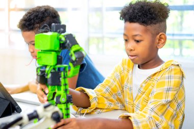 Afrika kökenli Amerikalı çocuklar sınıfa robot malzemeleri koyuyorlar. Robot sınıfında iki Amerikalı çocuk robot seti yapıyor..