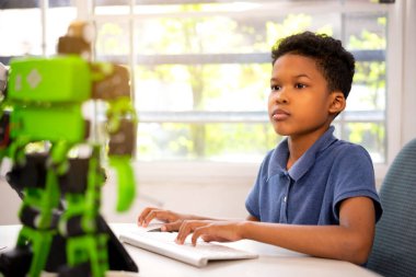 Afrikalı Amerikalı bir çocuk robot kiti programlıyor. Çocuk robot sınıfındaki robot setine program yüklüyor.