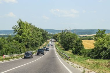 Resimli bir manzaranın arka planına karşı düz iki şeritli bir yol. Yol kenarındaki yeşillik. Yaz, seyahat, arabalar, yeşillik yanar. Fotoğraf, kır manzarası, Ukrayna