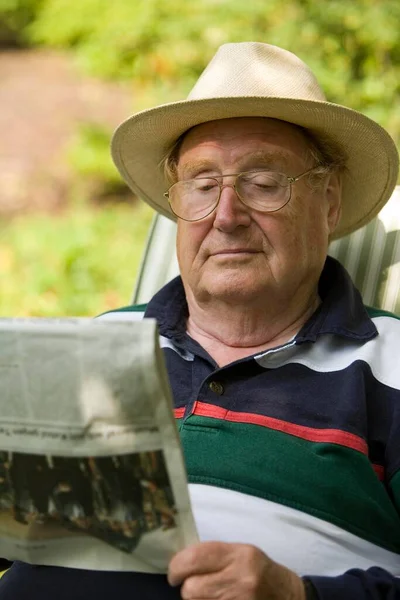 A relaxing senior citizen sitting in the garden reading a newspaper