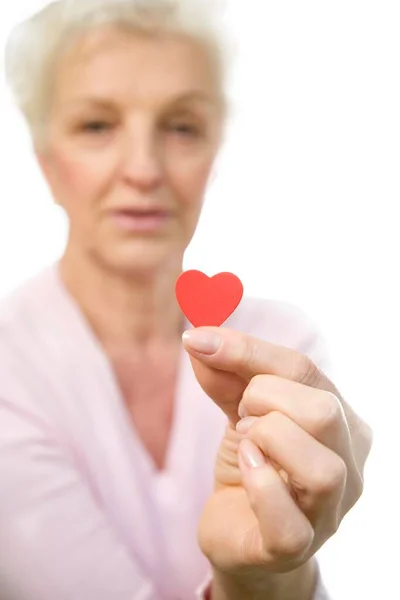 Зрелая Женщина Держит Красное Сердце Между Пальцами — стоковое фото