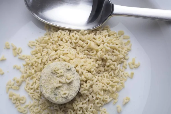 アルファベット麺に囲まれたプレート上の乾燥インスタントスープの塊 — ストック写真