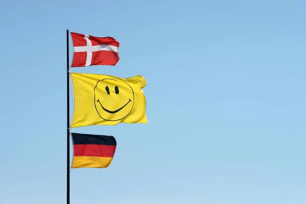 旗竿には笑顔の旗と共にドイツとデンマークの国旗が掲げられている — ストック写真