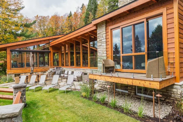 加拿大魁北克北美秋天的豪华色彩艳丽的雪松和木料屋背景图 配有全景窗 甲板和天然石料庭院 — 图库照片