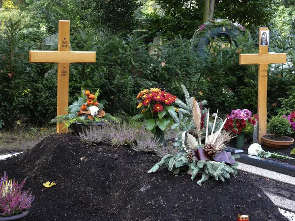 Wooden cross on fresh grave, cemetery in autumn on All Saints' Day, autumn flower arrangement, grave decoration for winter, fallen leaves in autumn