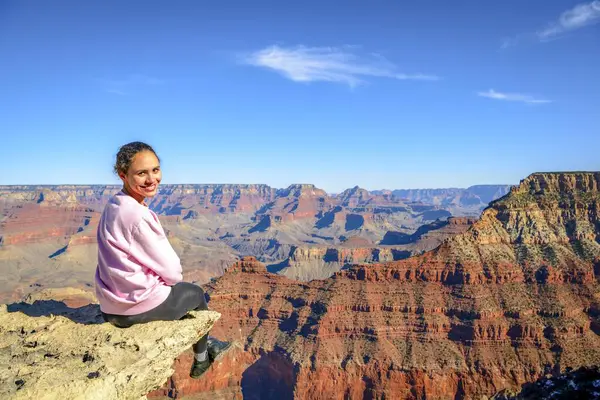 年轻的微笑的女人 坐在大峡谷的深渊边 从马特角和雅瓦佩角之间的环形山道上眺望 侵蚀着美国亚利桑那州土萨扬市附近的南缘 大峡谷国家公园和北爱美州的岩石景观 — 图库照片