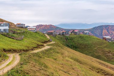Dağın tepesinde bulunan plato evleri. Arka planda karlı dağlar ve bulutlar.