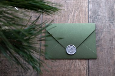 Balmumu mühür ve çam dallarıyla kaplı zeytin yeşili zarf..