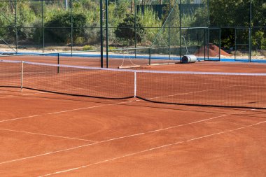 Güneşli bir günde boş bir kil tenis kortunun taban ve ağı