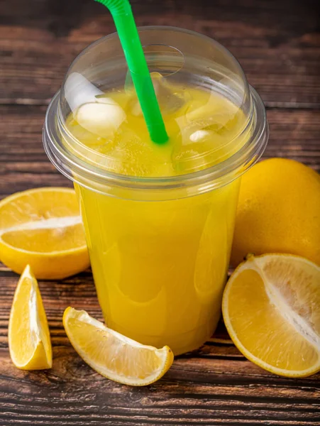 Lemonade in a take away glass with cut lemon next to it on wooden table