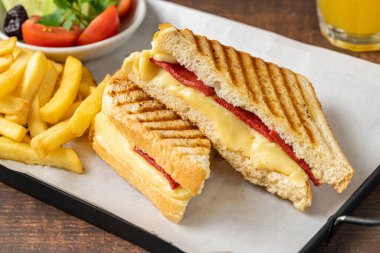 Çedar peynirli tost ve patates kızartmalı Türk sosisi ve ahşap masada salata.