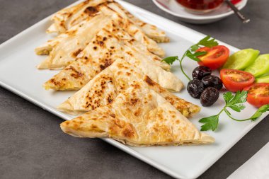 Geleneksel Türk yassı ekmeği veya domatesli, zeytinli ve koyu taş masada çay