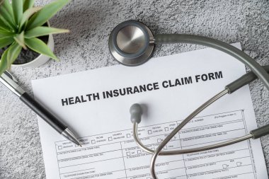Top view of doctor's stethoscope, pen and health insurance claim form on table