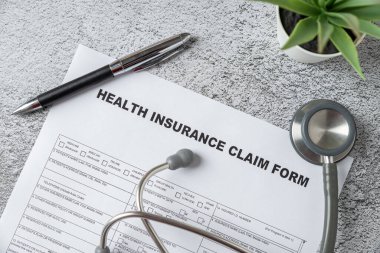 Top view of doctor's stethoscope, pen and health insurance claim form on table