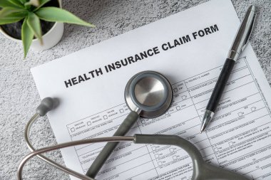 Top view of doctor's stethoscope, pen and health insurance claim form on table