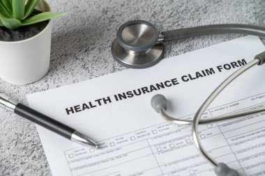 Top view of doctor's stethoscope, pen and health insurance claim form on table