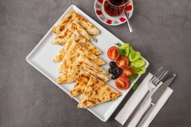 Geleneksel Türk yassı ekmeği veya domatesli, zeytinli ve koyu taş masada çay