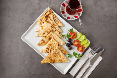 Geleneksel Türk yassı ekmeği veya domatesli, zeytinli ve koyu taş masada çay