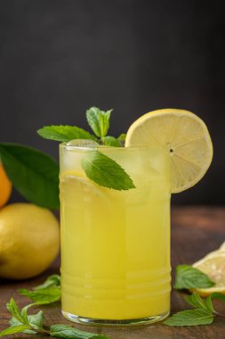 Taze nane yapraklı limonata ve ahşap masadaki cam bardakta limon dilimi.