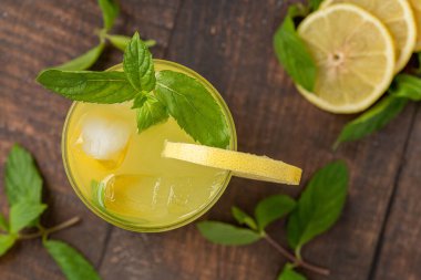 Taze nane yapraklı limonata ve ahşap masadaki cam bardakta limon dilimi.