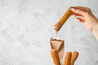 Bir kadın koniden churros alıp çikolata sosuna batırıyor.