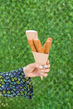 Yeşil çim duvarın önündeki karton kutuda churros tutan kadın.