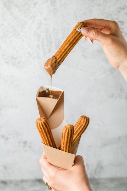 Bir kadın koniden churros alıp çikolata sosuna batırıyor.