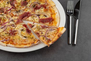 Pastırma ve mantarlı pizza. Taş masada porselen tabakta.