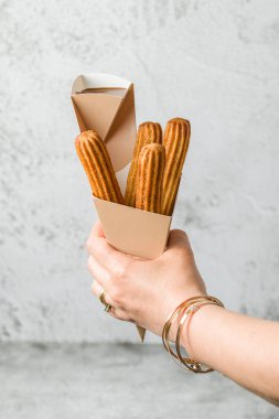 Bir kadın koniden churros alıp çikolata sosuna batırıyor.