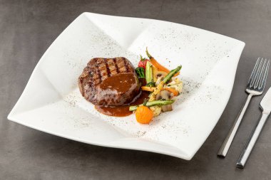 Beyaz porselen tabakta ızgara sebzeli Demi glace soslu ızgara sığır filetosu.