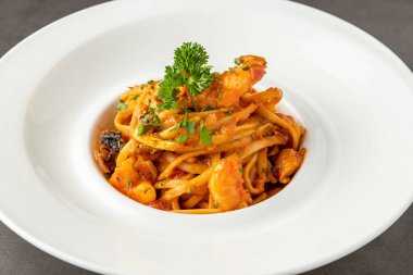 Siyah taş masadaki beyaz porselen tabakta karides spagettisi.