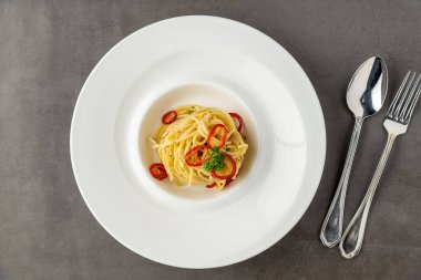 Paprikalı spagetti, beyaz porselen tabakta, siyah taş masada.