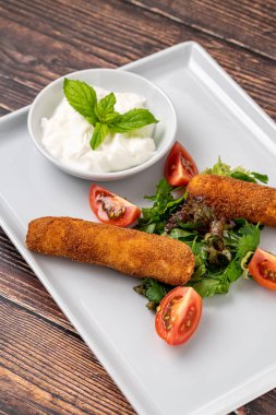 Beyaz porselen tabakta yeşil ve soslu Mozzarella çubukları.