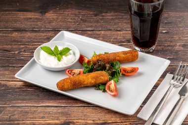 Beyaz porselen tabakta yeşil ve soslu Mozzarella çubukları.