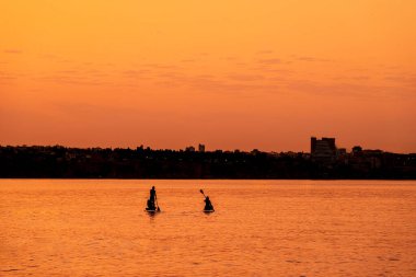 Ayakta duran maceraperest insanlar parlak ve canlı bir gündoğumunda kürek çekiyorlar.