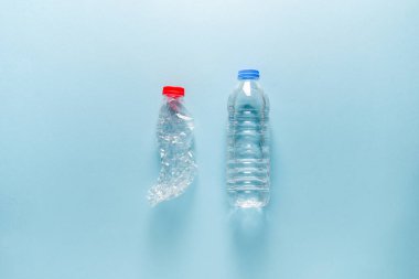 Boş ve ezilmiş plastik su şişesiyle dolu plastik su şişesi mavi arka planda yan yana duruyor.