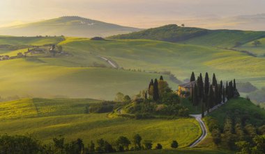 İtalya, San Quirico d 'Orcia' da gündoğumunda Val d 'Orcia vadisinin sisli sabah güneşli tepeleri arasında selvi ağaçlarıyla çevrili bir ev.